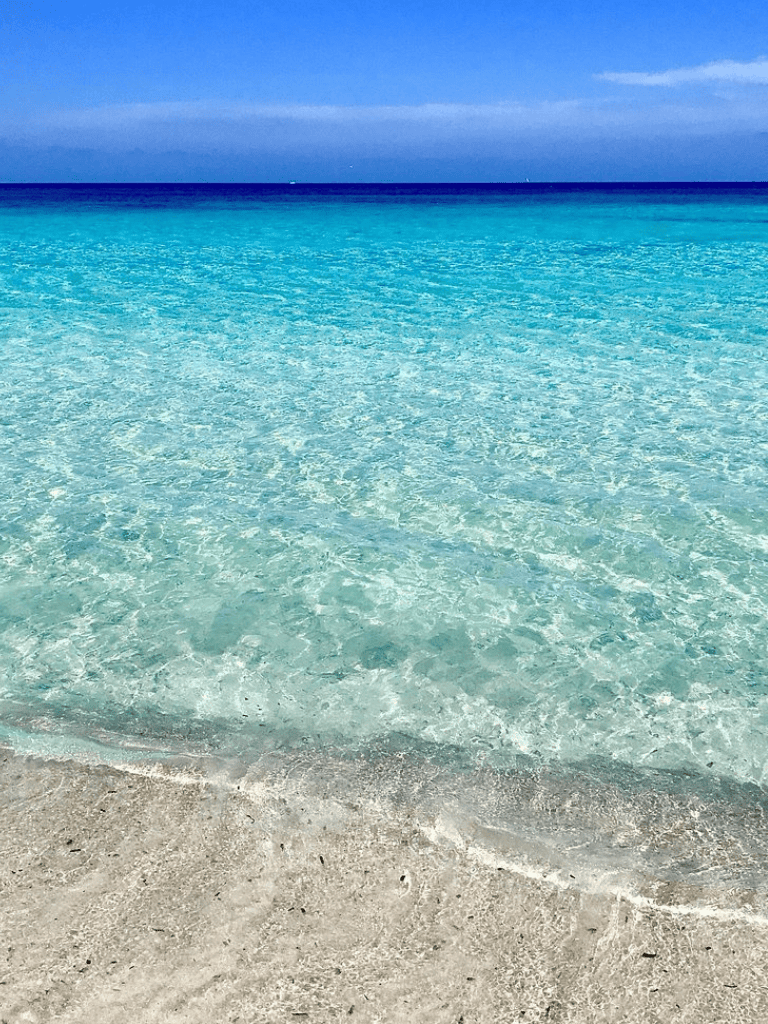 Crystal clear tropical ocean water at beach with white sand shoreline.
