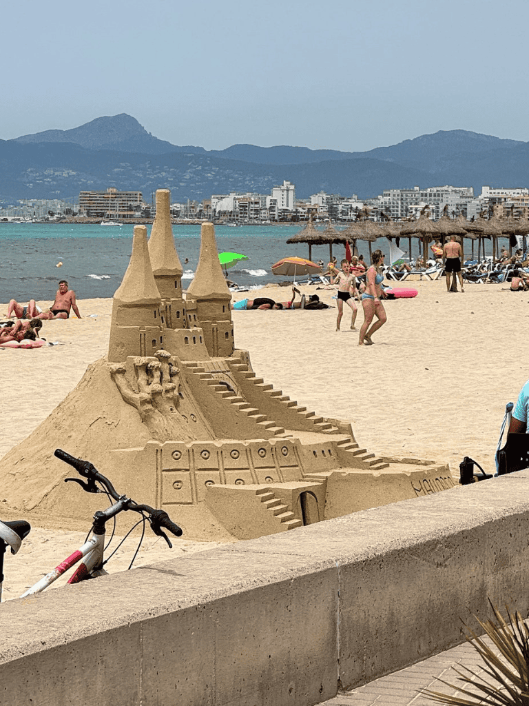 - Intricate sandcastle on a beach with visitors, umbrellas, and ocean view in the background.