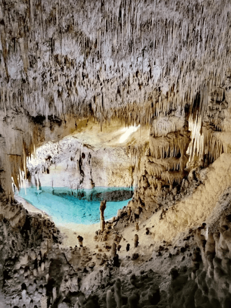 Vivid image of a stunning underground cave featuring a crystal-clear turquoise lake with stalactites and stalagmites.