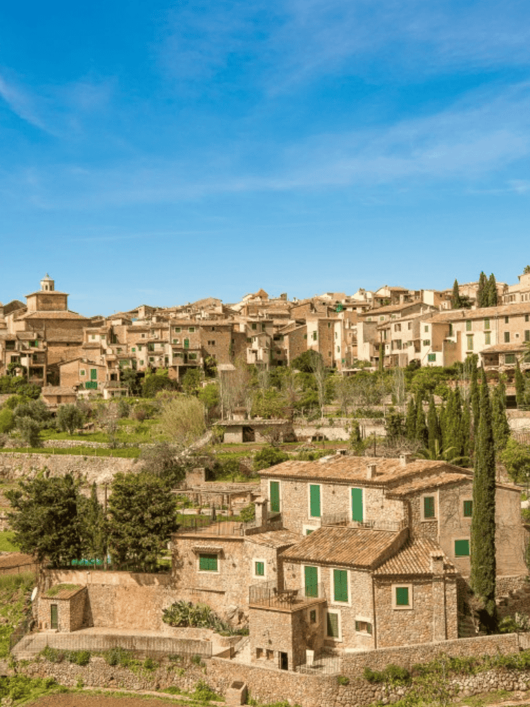 Charming hillside Italian village with stone houses and lush greenery under a clear blue sky.