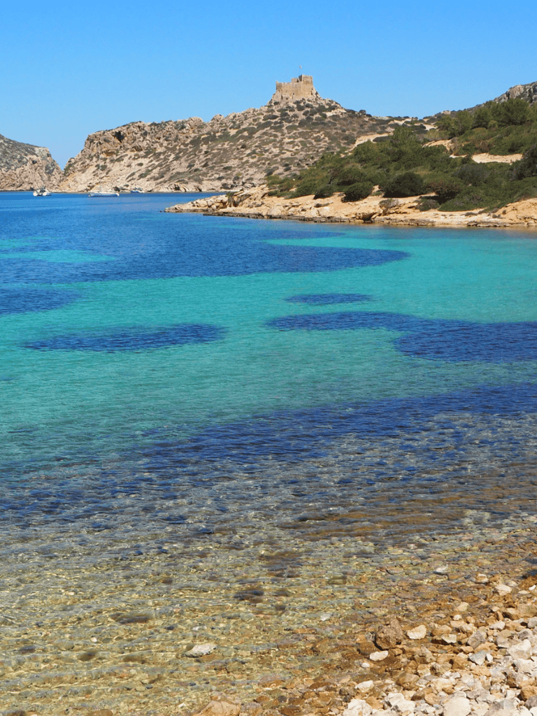 Stunning coastal landscape with clear turquoise waters and historic castle in the background.