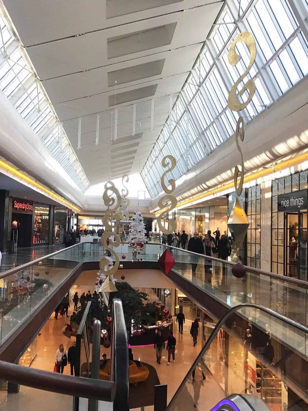 Bright indoor shopping mall decorated for Christmas with hanging ornaments and a Christmas tree.
