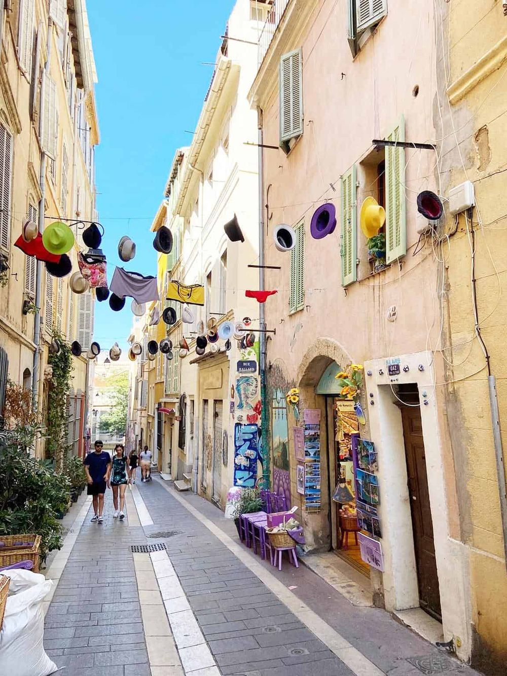 Colorful narrow street in Nice, France with hanging hats and street art, perfect for exploring local culture.