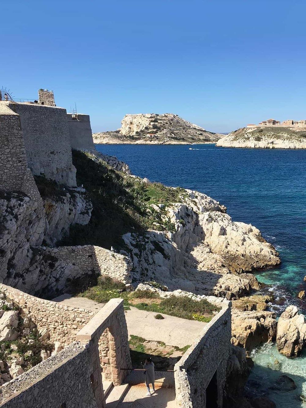 Scenic coastal view of a rocky shoreline with historic stone structures and a deep blue sea under clear skies.
