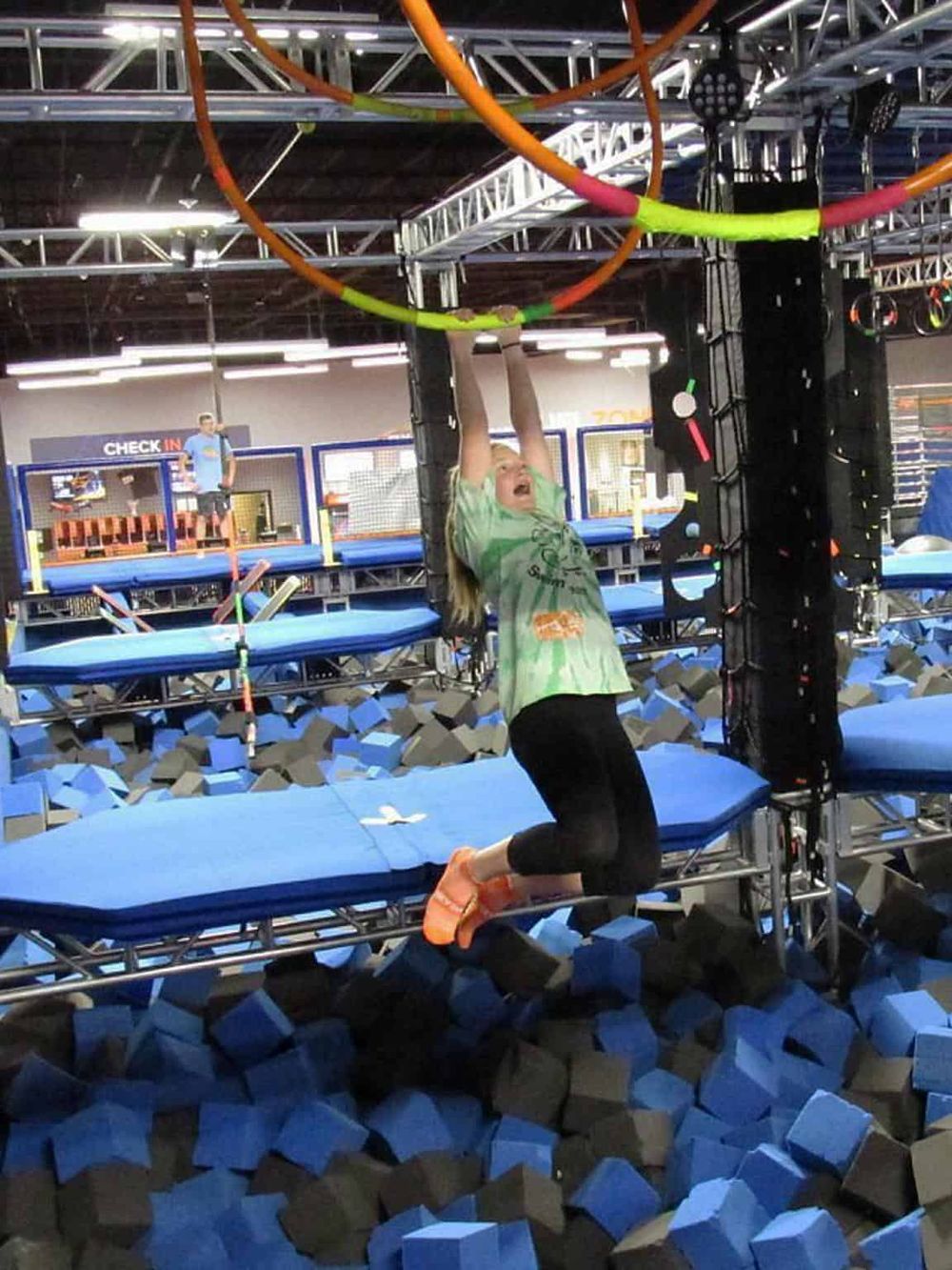 Child hanging from indoor trampoline park obstacle course, enjoying active fun and adventure at Quest for Directions.
