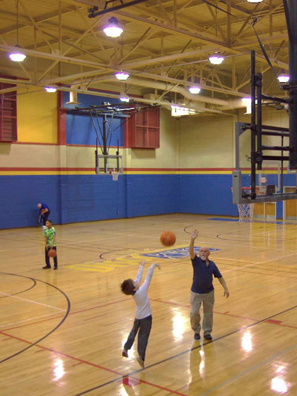 Indoor basketball gymnasium with players practicing shots and drills, featuring vibrant wall colors and professional equipment.