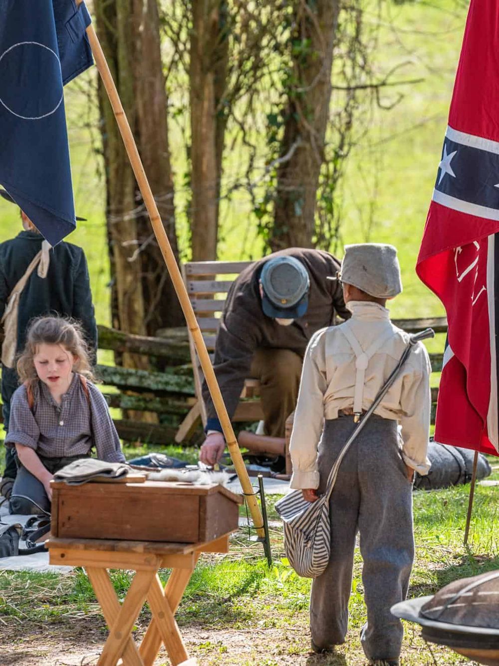 Outdoor historical reenactment with children in vintage costumes in a lush green forest setting.