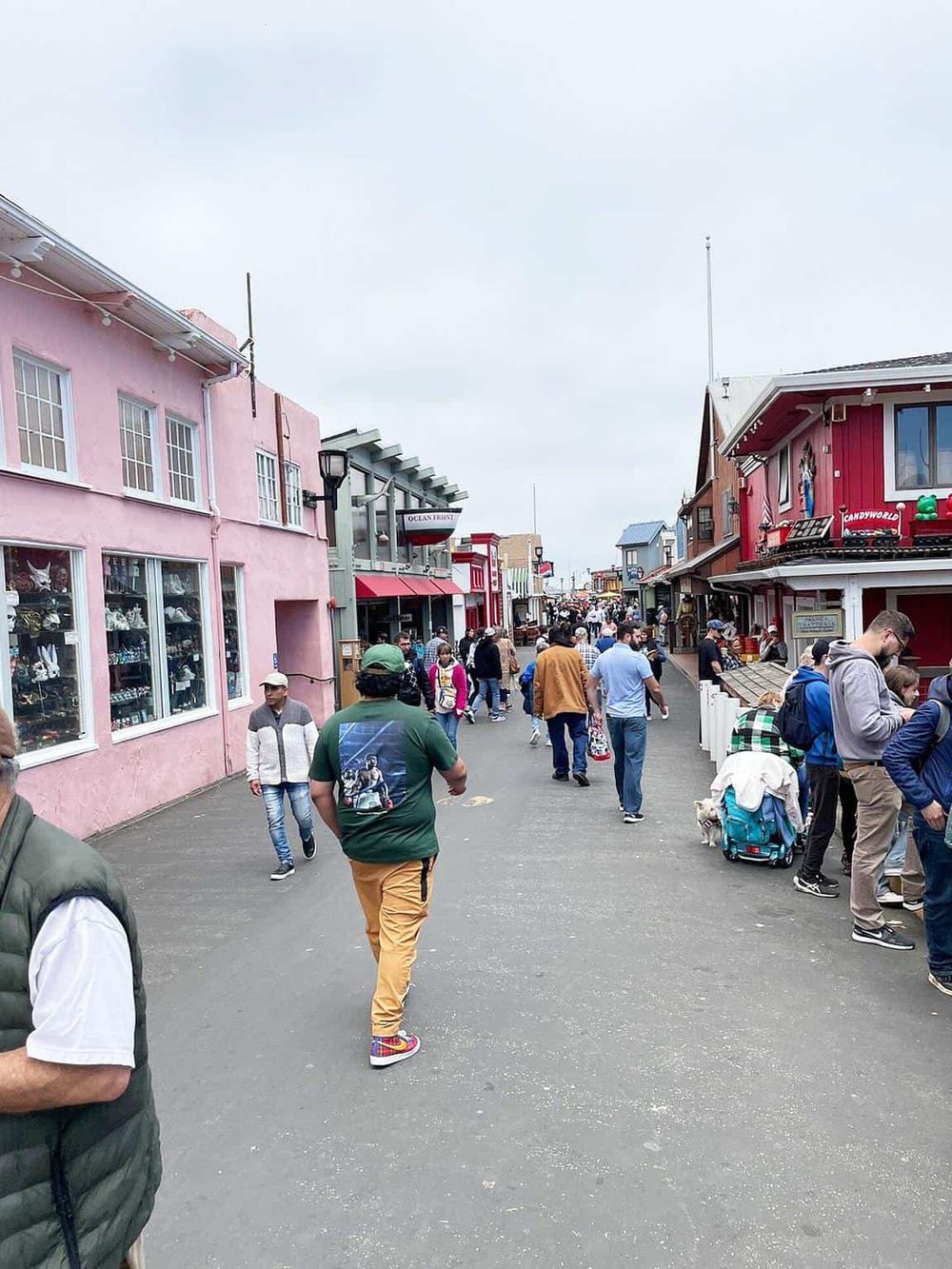Colorful seaside shopping street with shops and pedestrians at an outdoor tourist attraction.