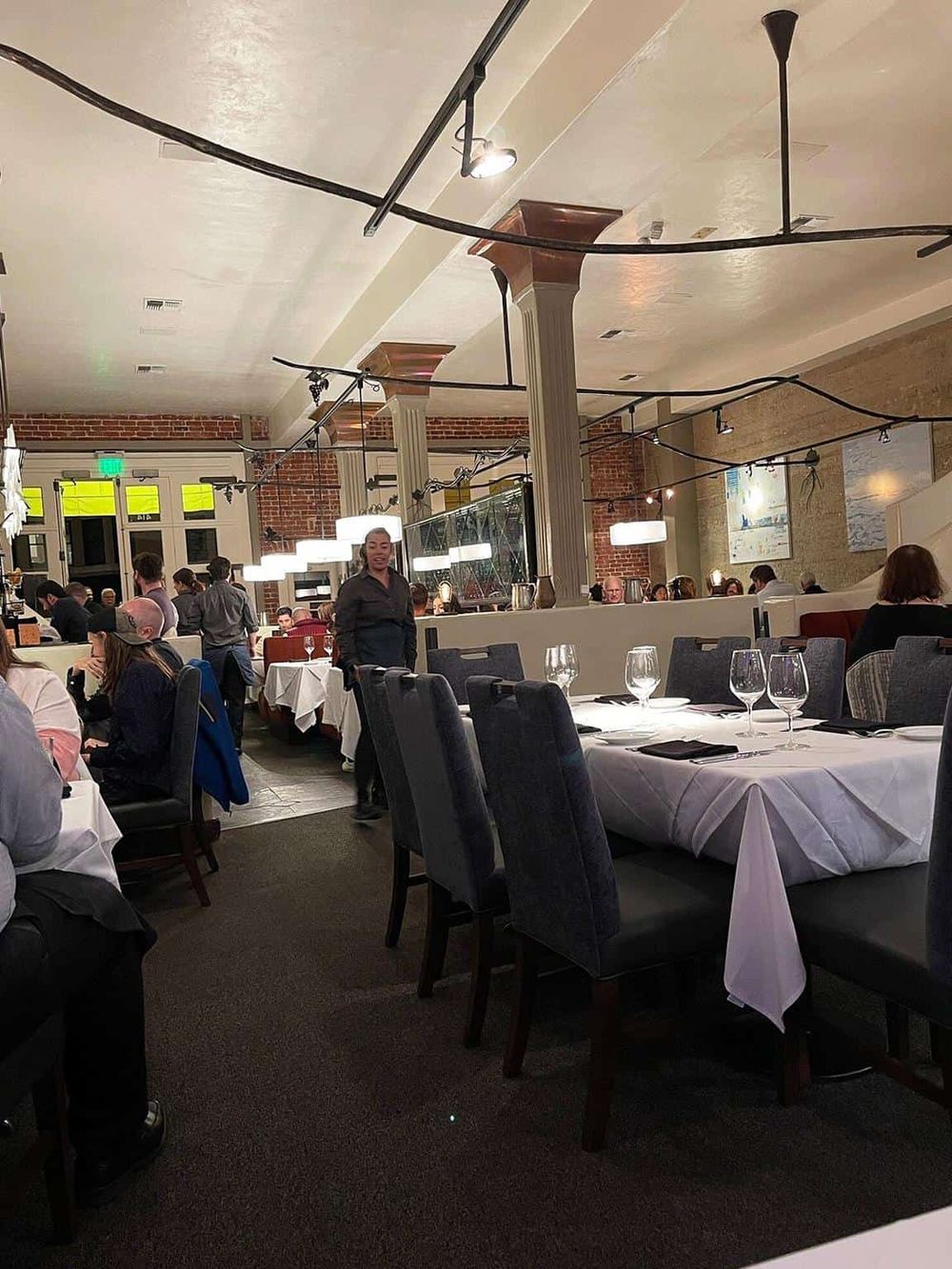 Elegant restaurant interior with white tablecloths, modern lighting, and diverse guests dining.
