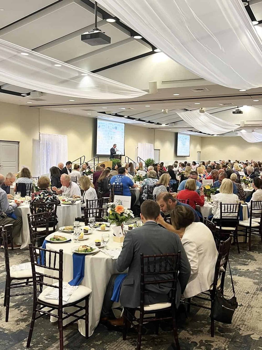 Elegant banquet hall with guests enjoying a conference dinner and presentation, showcasing event planning and hospitality services.