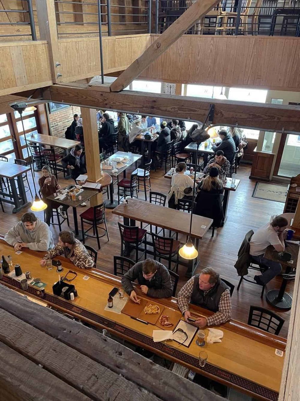 Cozy restaurant interior with wooden beams, casual dining atmosphere, and customers enjoying meals and drinks.