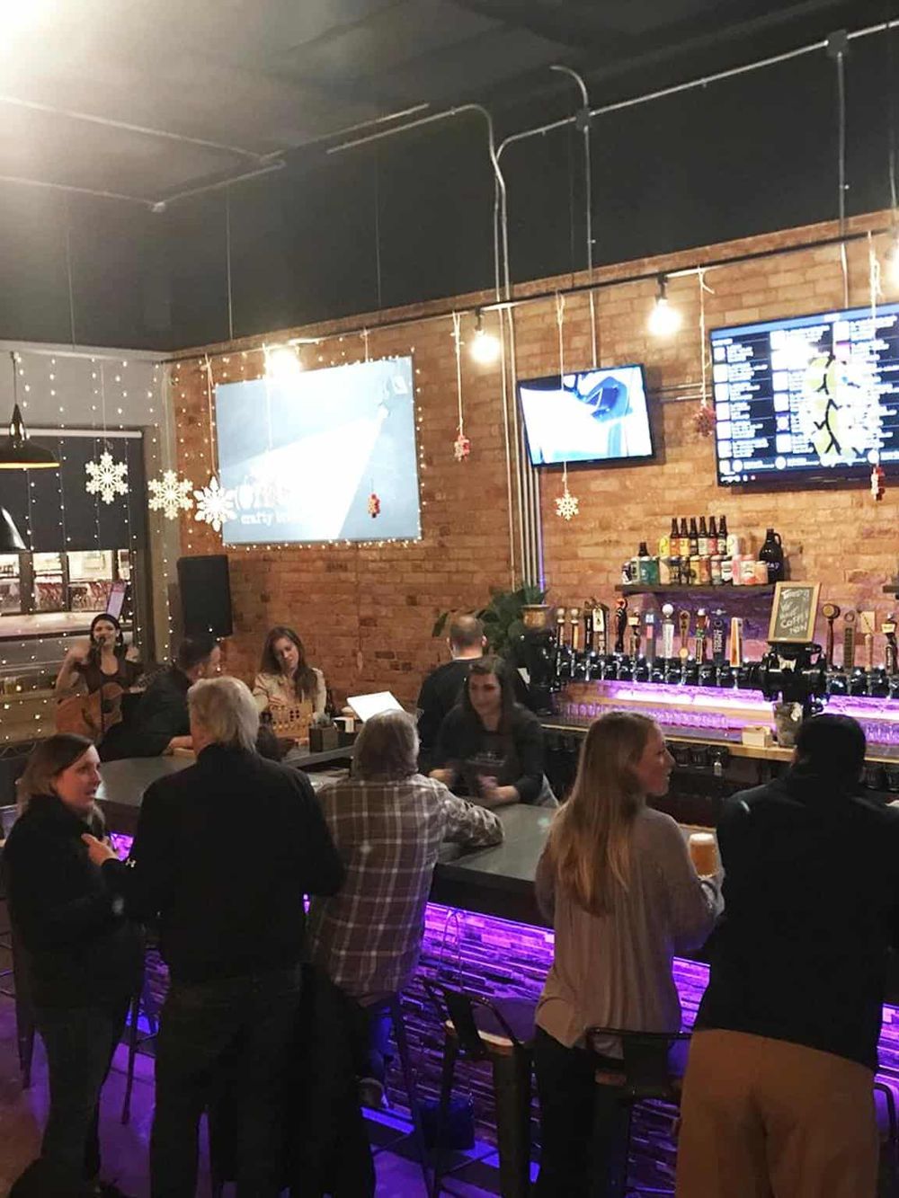 Cozy bar and lounge with people enjoying drinks, live music, and festive holiday decorations in a brick-walled setting.