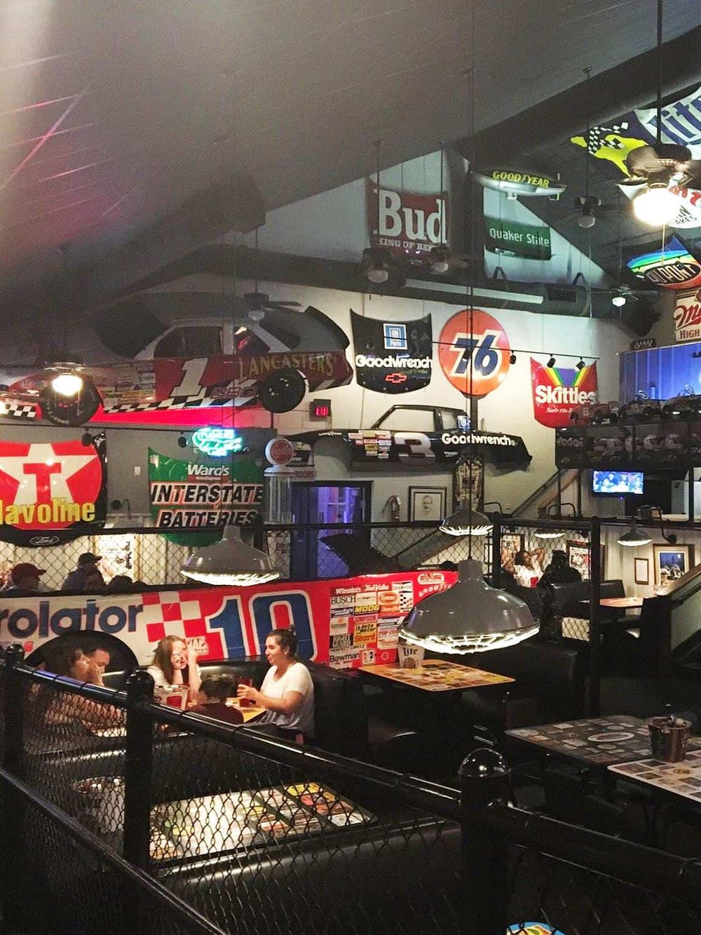 Vast indoor racing-themed restaurant with vintage car and automotive signs, lively atmosphere, and group dining experience.