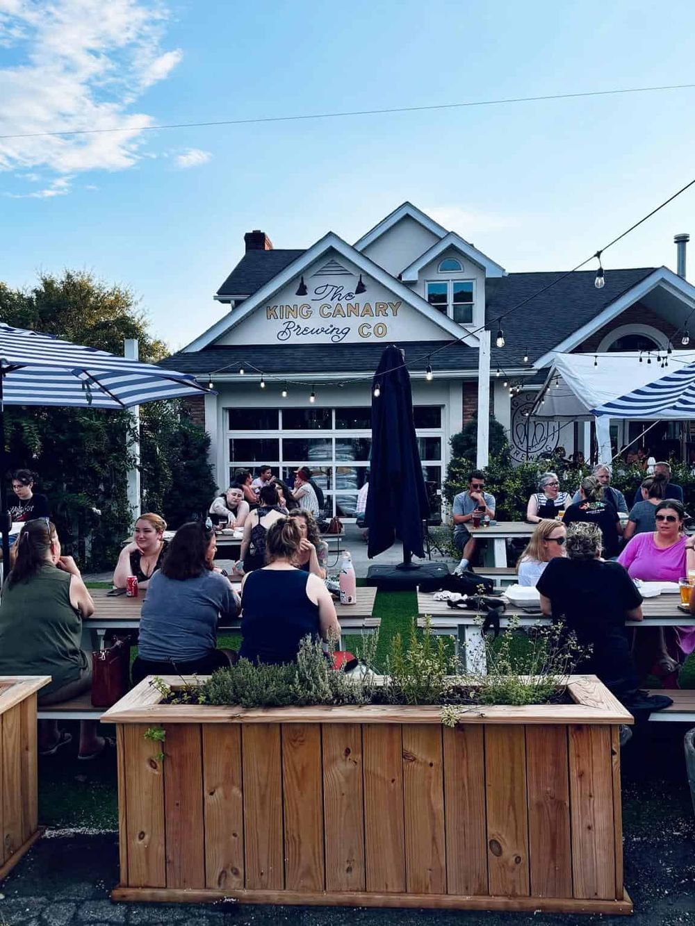 Outdoor beer garden at The King Canary Brewing Co. with patrons enjoying drinks and food.