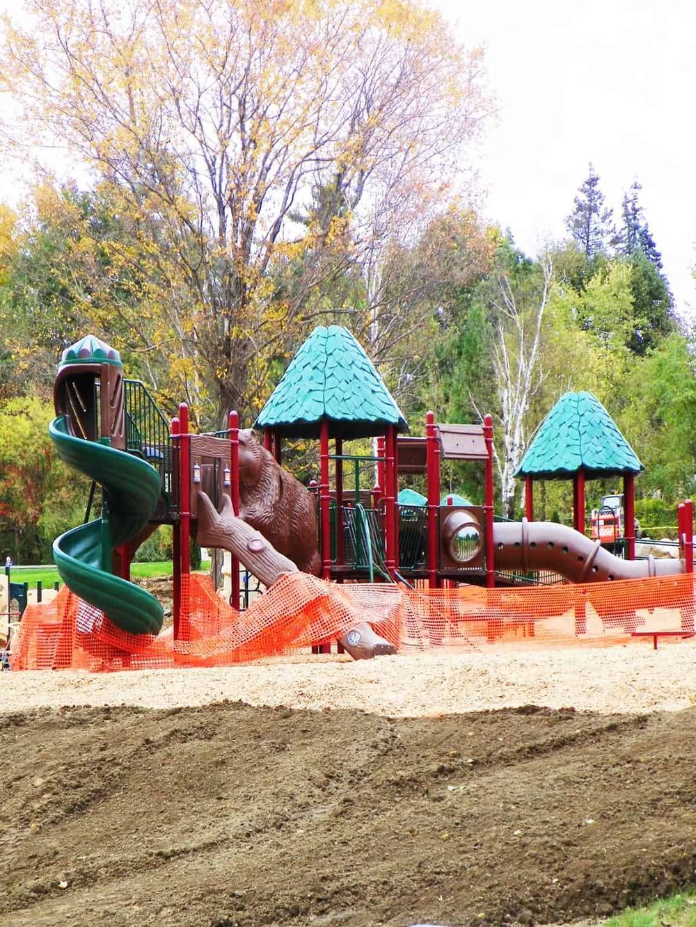 Colorful children's playground with slides and tunnels, surrounded by trees in fall.