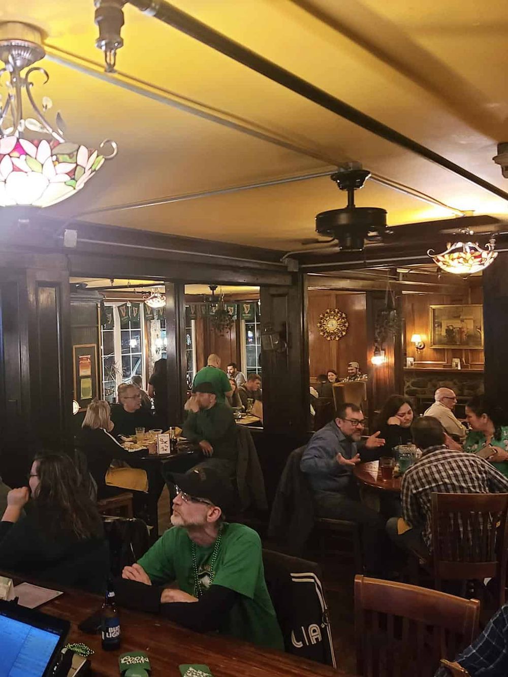 Cozy pub interior with groups of people enjoying food and drinks, warm lighting, and rustic wooden decor.