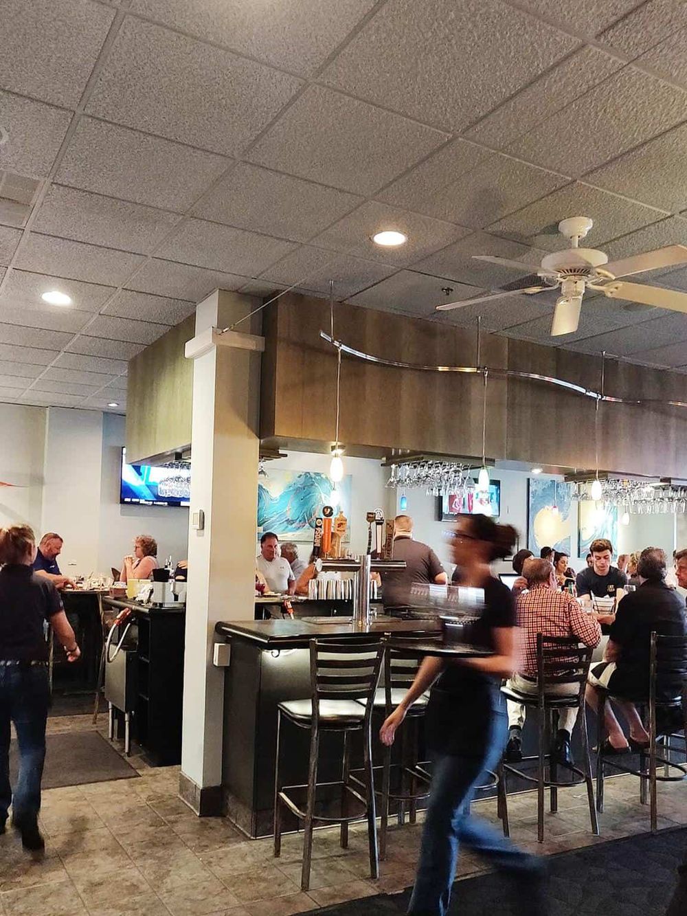 Cozy restaurant interior with busy patrons, bar area, modern decor, and overhead lighting for a welcoming dining atmosphere.