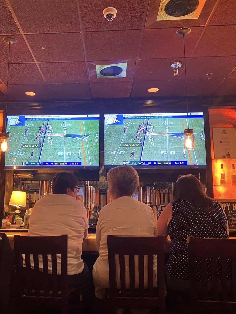 Watching football game at sports bar with multiple screens, lively atmosphere, and people enjoying drinks.