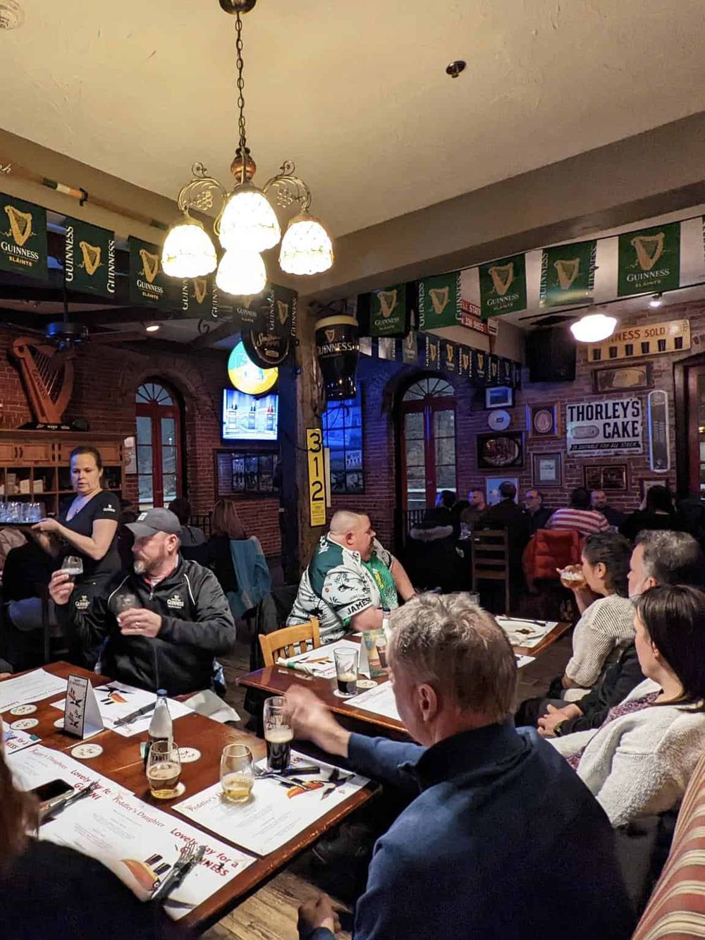Warm pub interior with people enjoying drinks and conversation, Irish-themed decor, and Guinness banners.