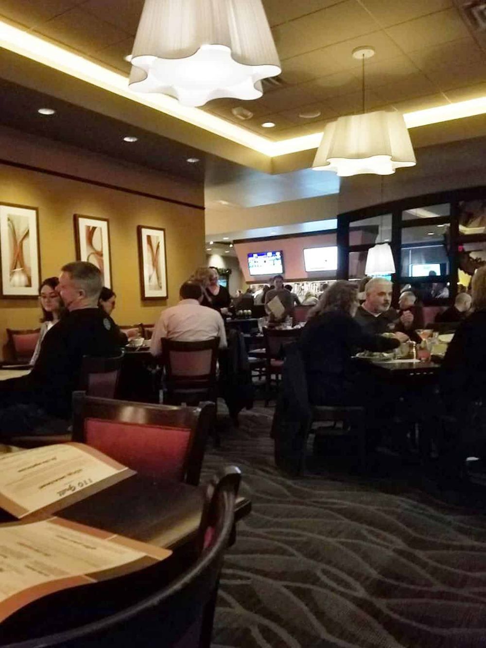 Cozy restaurant interior with diners, modern lighting, and TV screens, ideal for dining out and socializing.