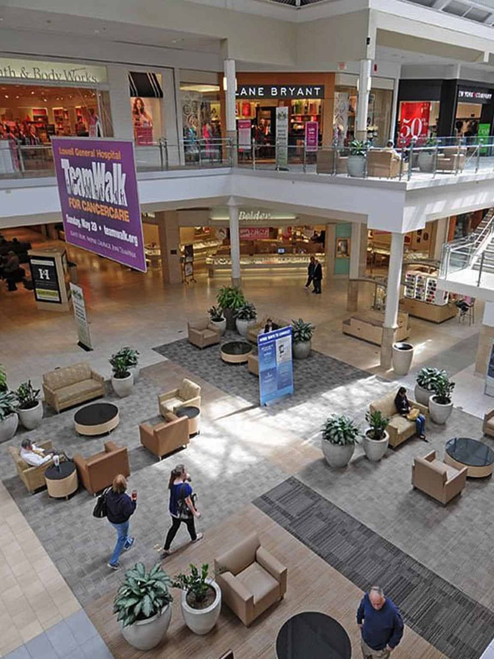 Bright indoor shopping mall with seating areas, store signs, and shoppers, capturing a vibrant retail environment.