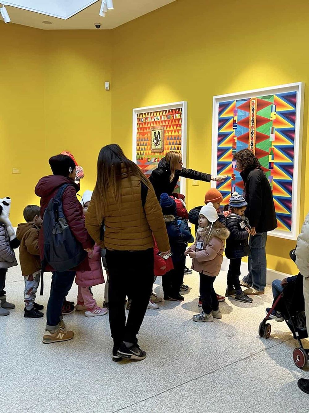 Colorful art gallery with children and adults observing vibrant geometric paintings, exploring creative artwork at QuestForDirections.