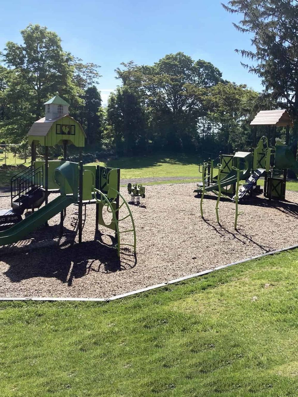 Bright green playground equipment at an outdoor park with trees and grassy areas.