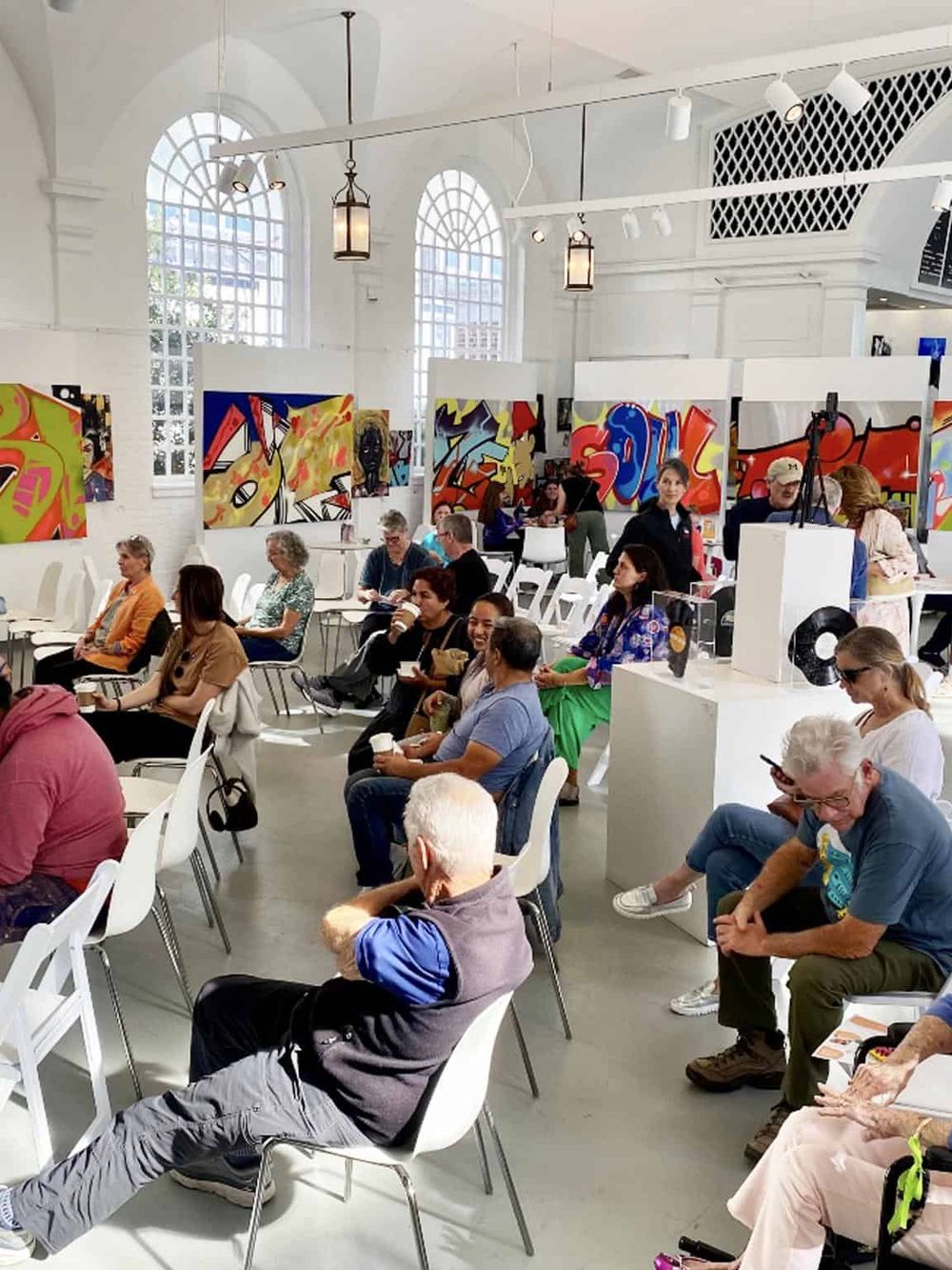 Colorful art gallery at QuestForDirections with visitors seated and engaging in the event.