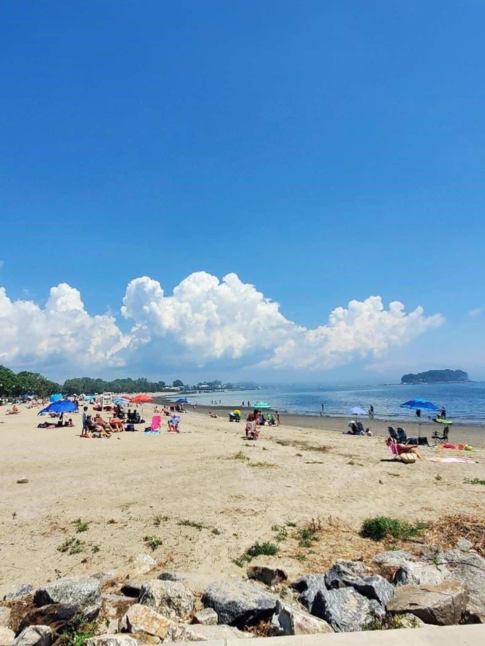 People relaxing and enjoying sunny day at sandy beach with colorful umbrellas and bright blue sky.