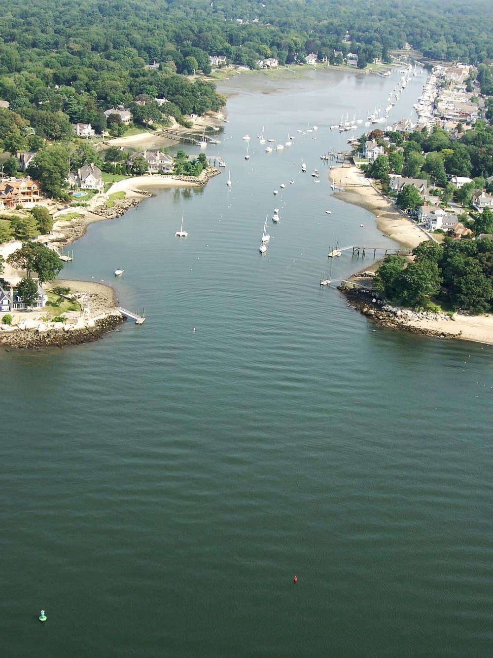 Aerial view of a scenic harbor with boats and waterfront homes in a coastal town.