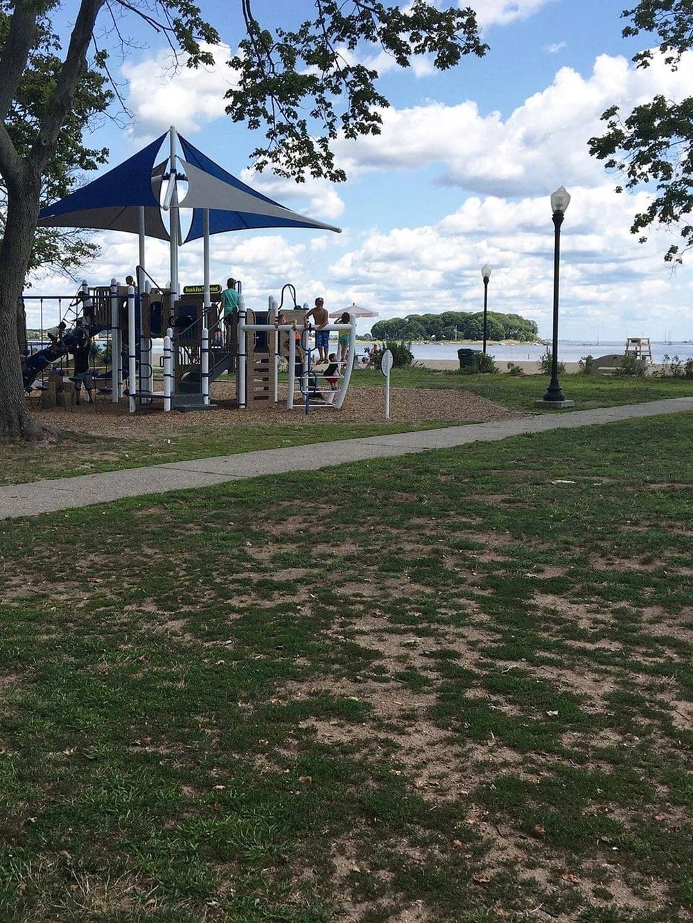 A playground by the water at Quest for Directions, with trees, a walking path, and scenic lake views.