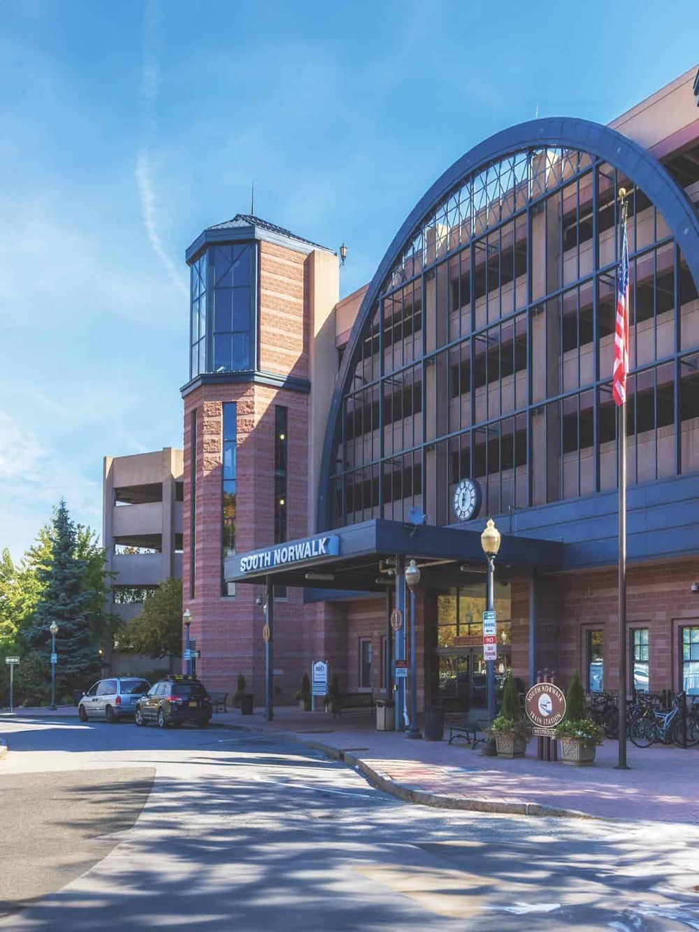 Modern building entrance with "South Norwalk" signage in a vibrant downtown area, featuring glass architecture and surrounding greenery.