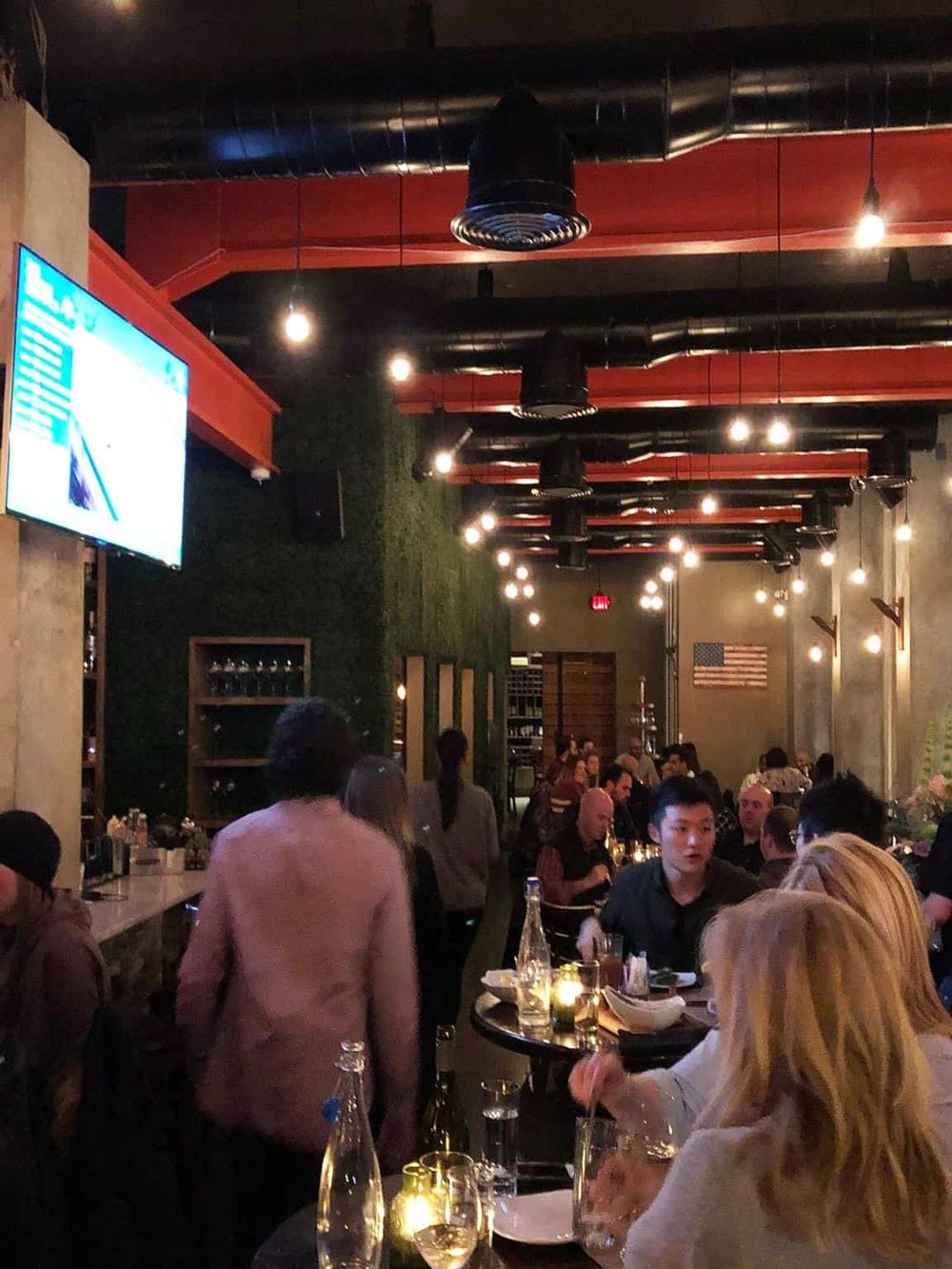 Stylish modern restaurant interior with dim lighting, high ceilings, and diverse patrons enjoying dining experience.