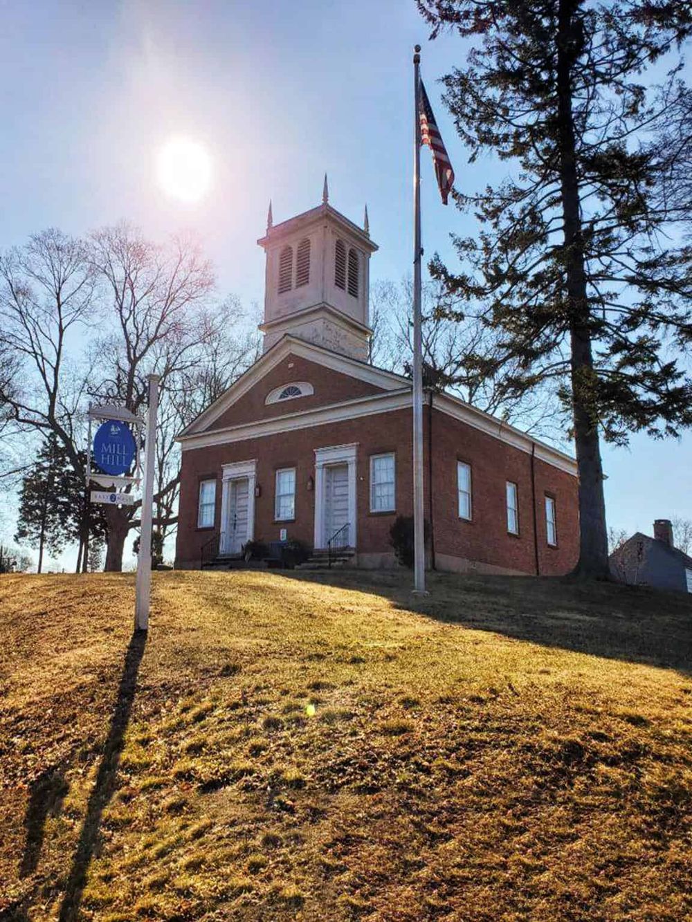 Beautiful historic brick church with white accents, American flag, and surrounding trees under bright sun for local directions.