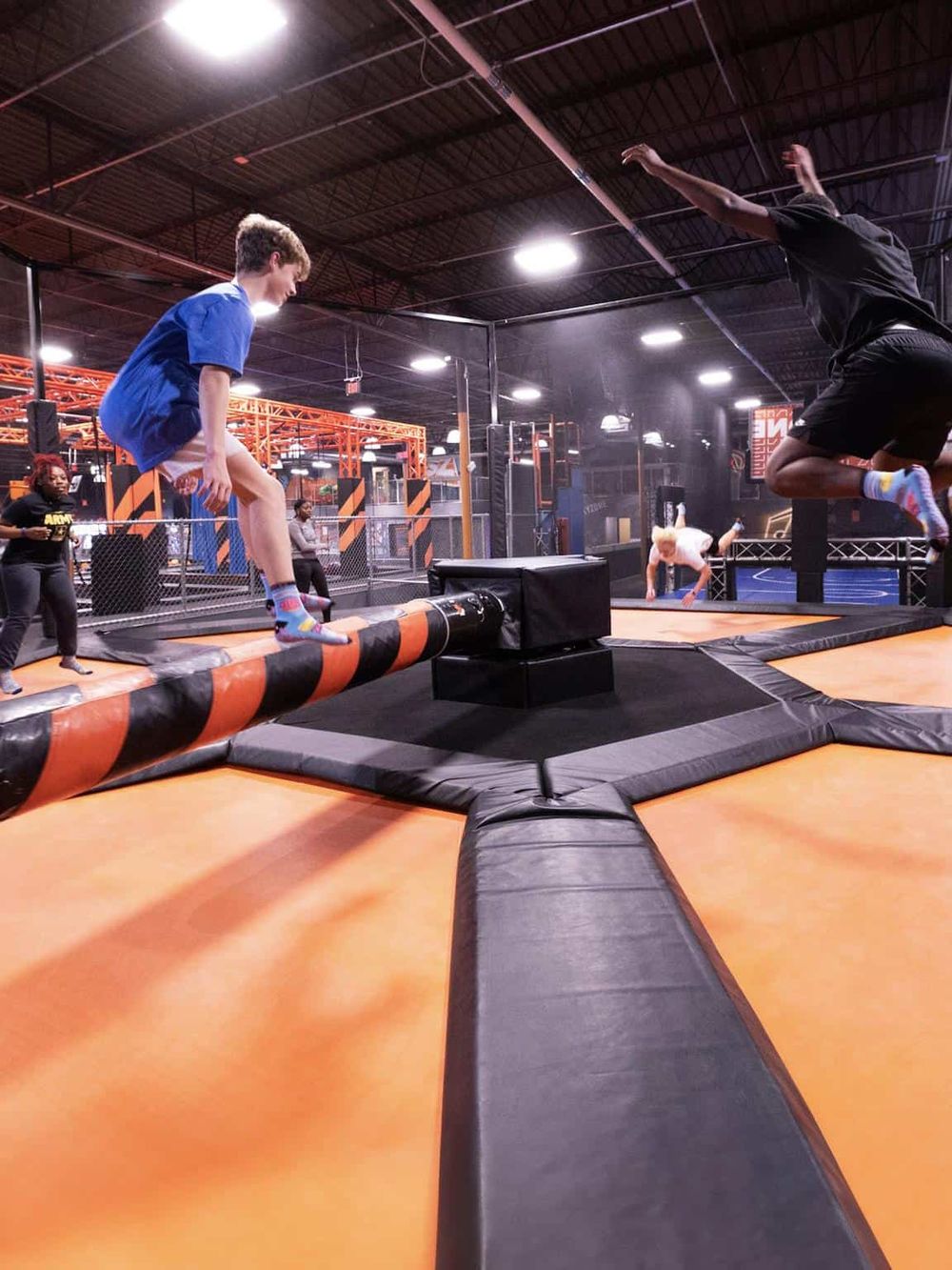 Climbing inside an indoor trampoline park with children jumping and playing on interconnected trampolines.