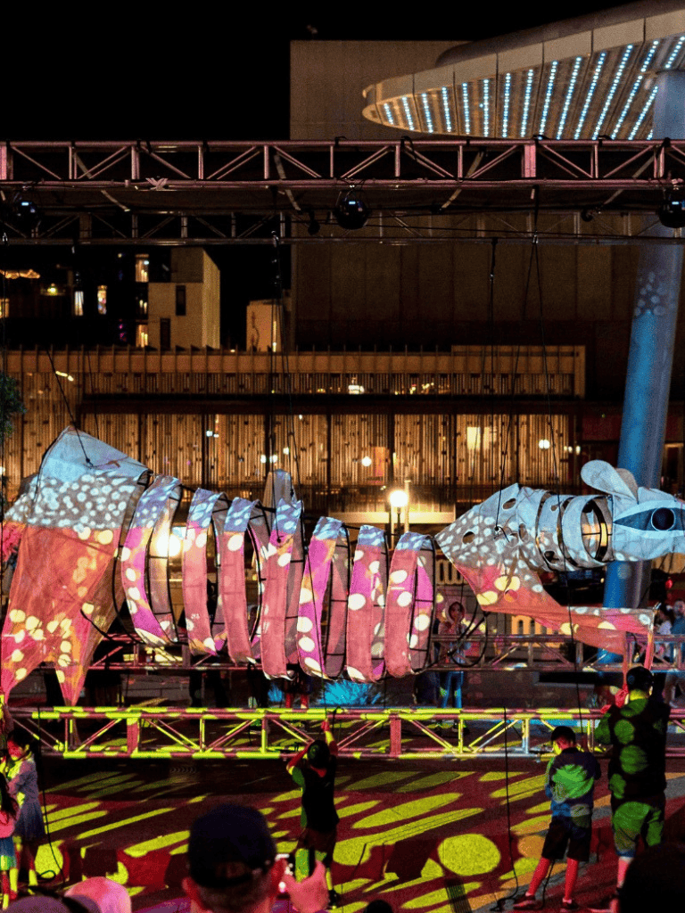 Colorful illuminated fish lantern at night during the QuestForDirections event, vibrant light projections and spectators enjoying the festival.