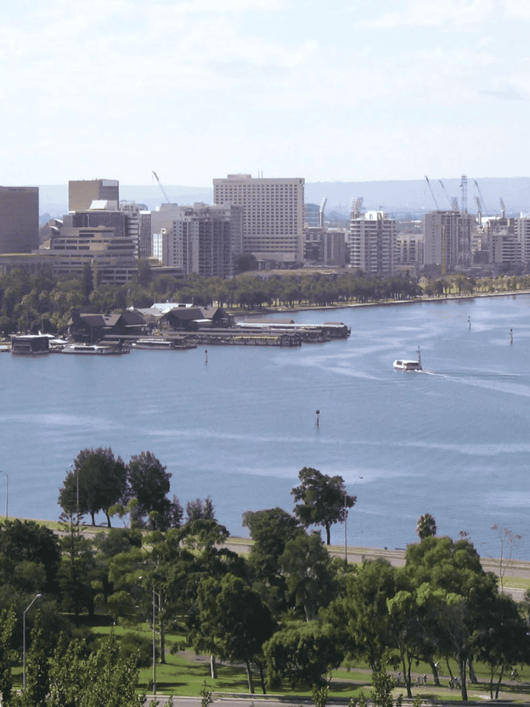 Vibrant city skyline with river and park in the foreground, showcasing urban and natural scenery.