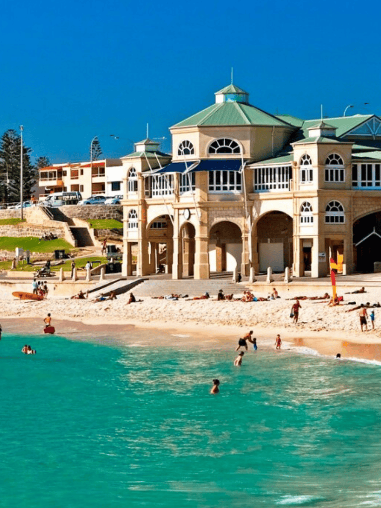 Relaxing beach scene with historic seaside building and people swimming in turquoise water.
