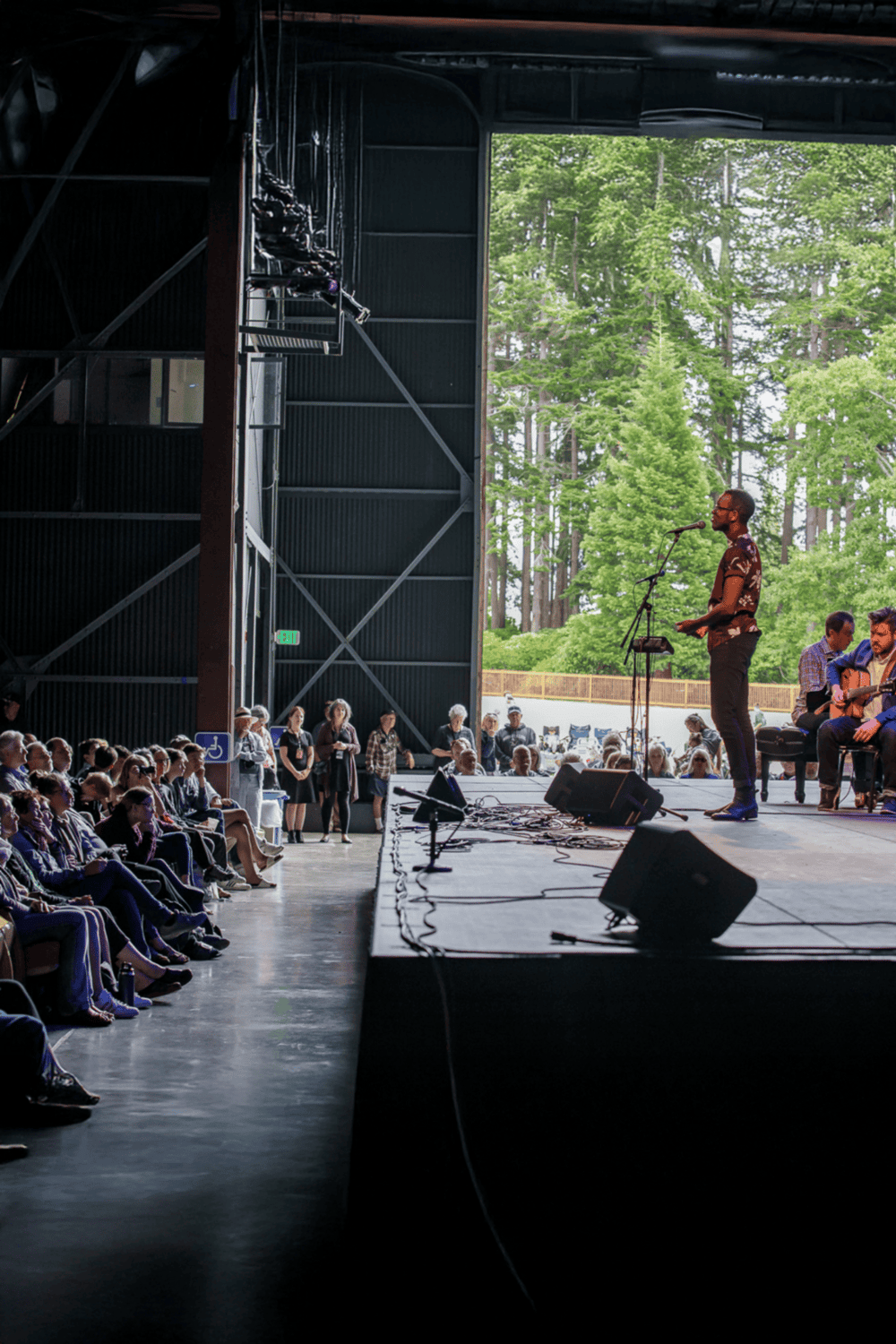 Indoor concert performance at QuestForDirections event with audience and outdoor scenery in the background.