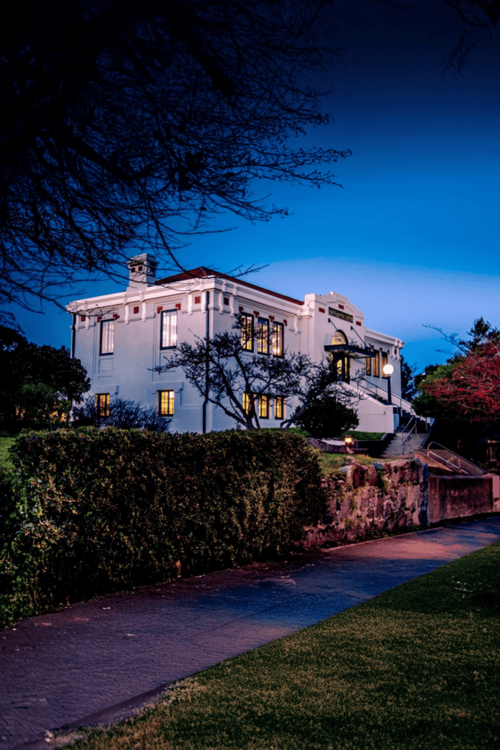 Modern historic house in a scenic neighborhood at dusk, illuminated windows, lush landscaping.