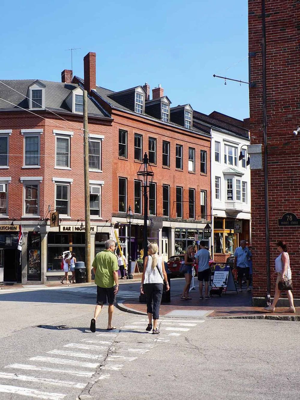 Colorful city street with brick buildings, pedestrians, and storefronts in a lively urban environment.