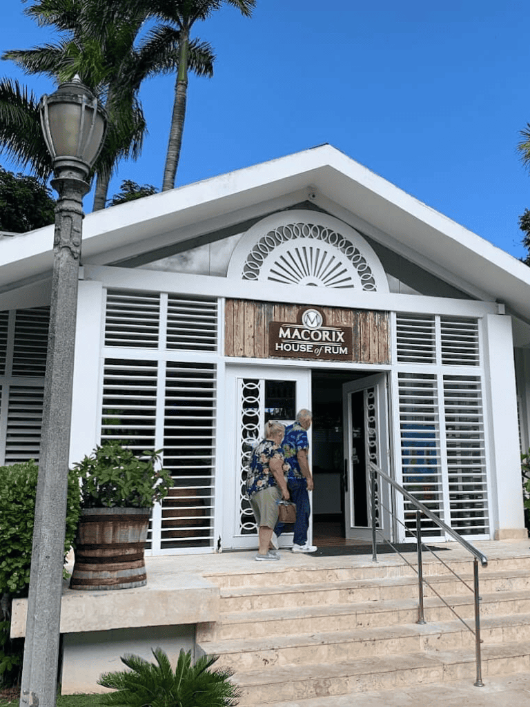 Elegant tropical resort entrance at Macorix House of Rum with guests entering, surrounded by palm trees and clear blue sky.