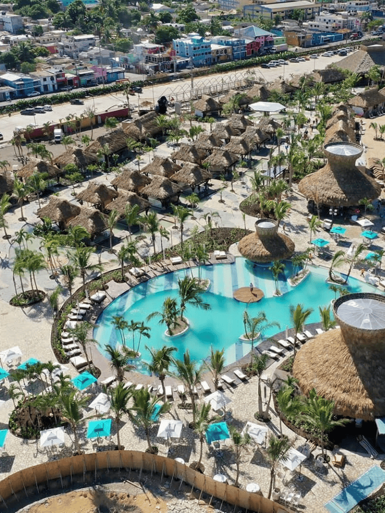 Luxurious resort with pool, thatched-roof huts, and tropical landscaping in a coastal setting.