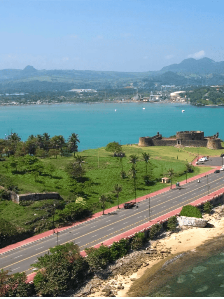 Scenic coastal view with historic fort, lush greenery, and turquoise waters in Puerto Rico.