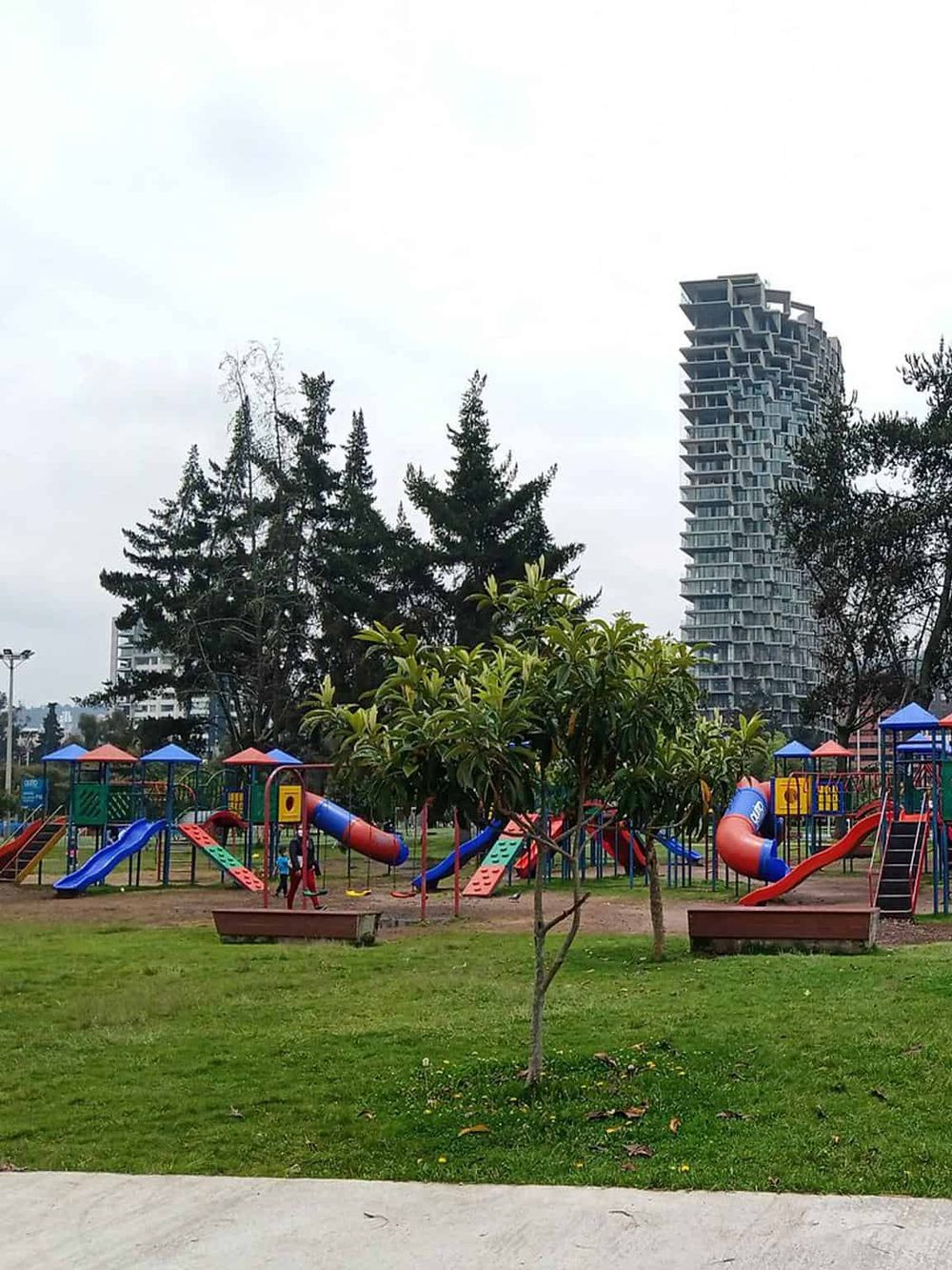 Colorful children’s playground with slides and tunnels at a park in front of tall modern residential buildings.