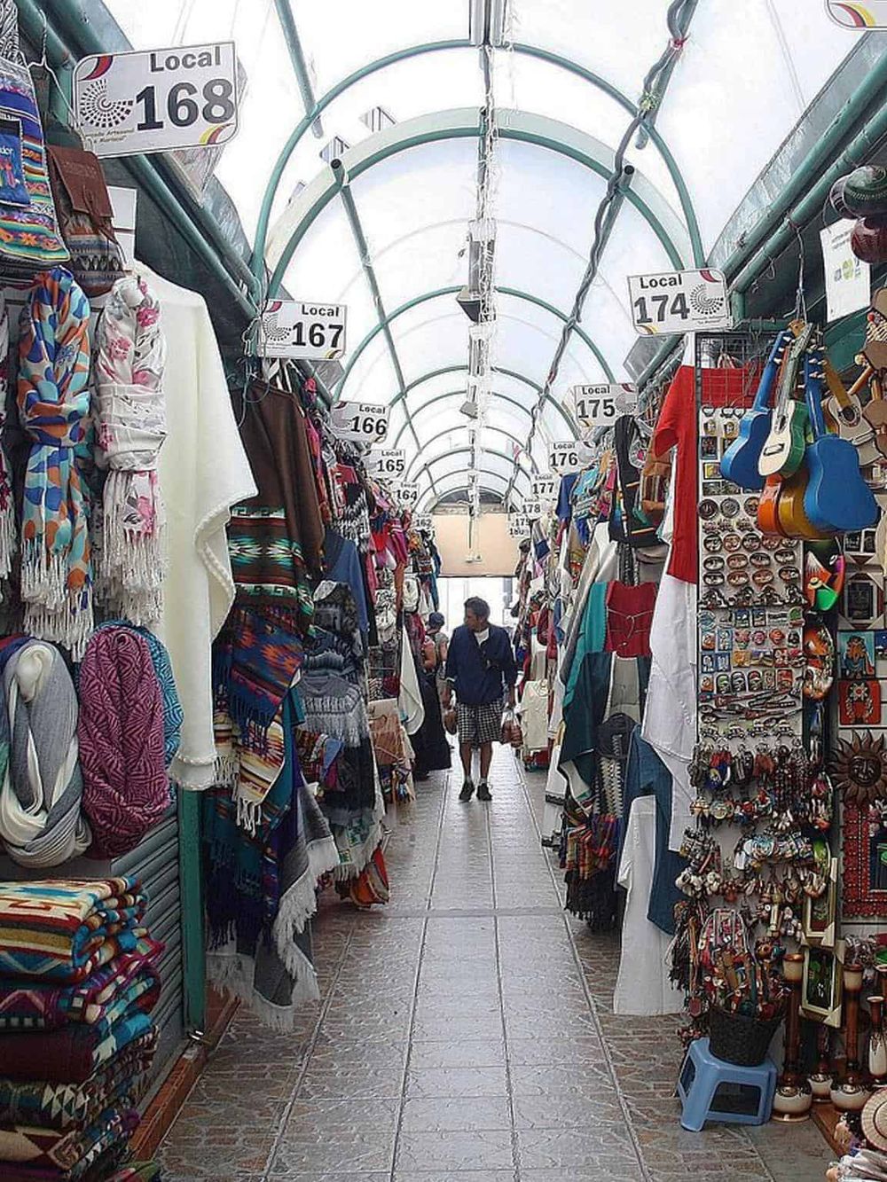 Colorful marketplace stalls with local souvenirs on display in a covered shopping alley.