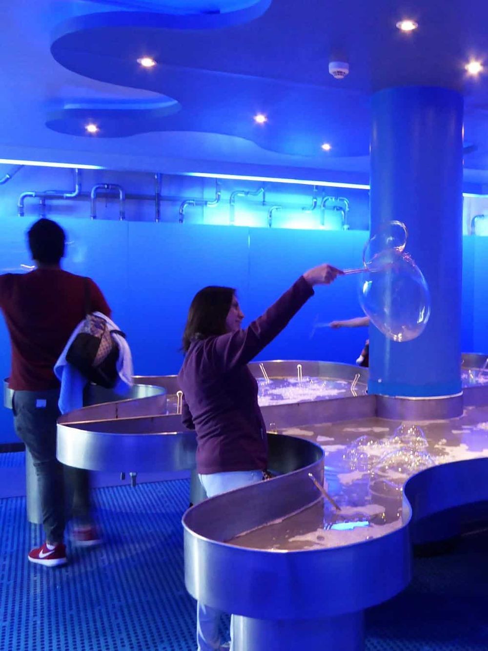 Bright blue-lit aquarium with people enjoying interactive marine exhibits and bubble displays.
