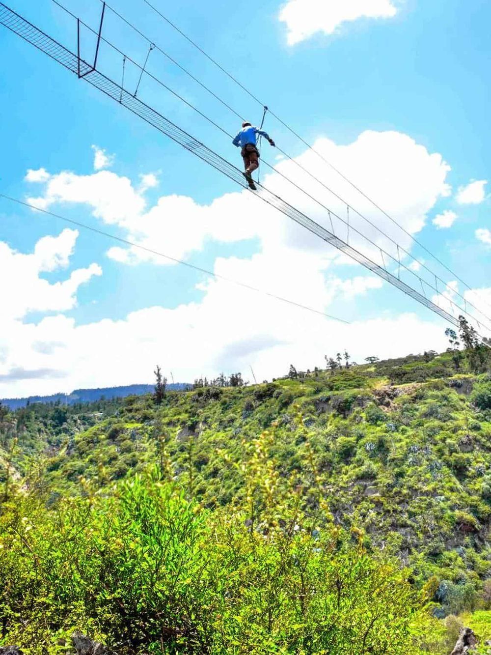 High ropes adventure course in lush green landscape with sky and clouds in background.