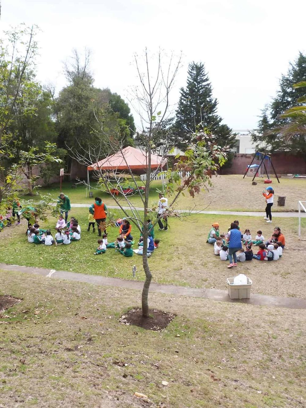 Outdoor children's playground with kids and teachers, educational activities, and swings.