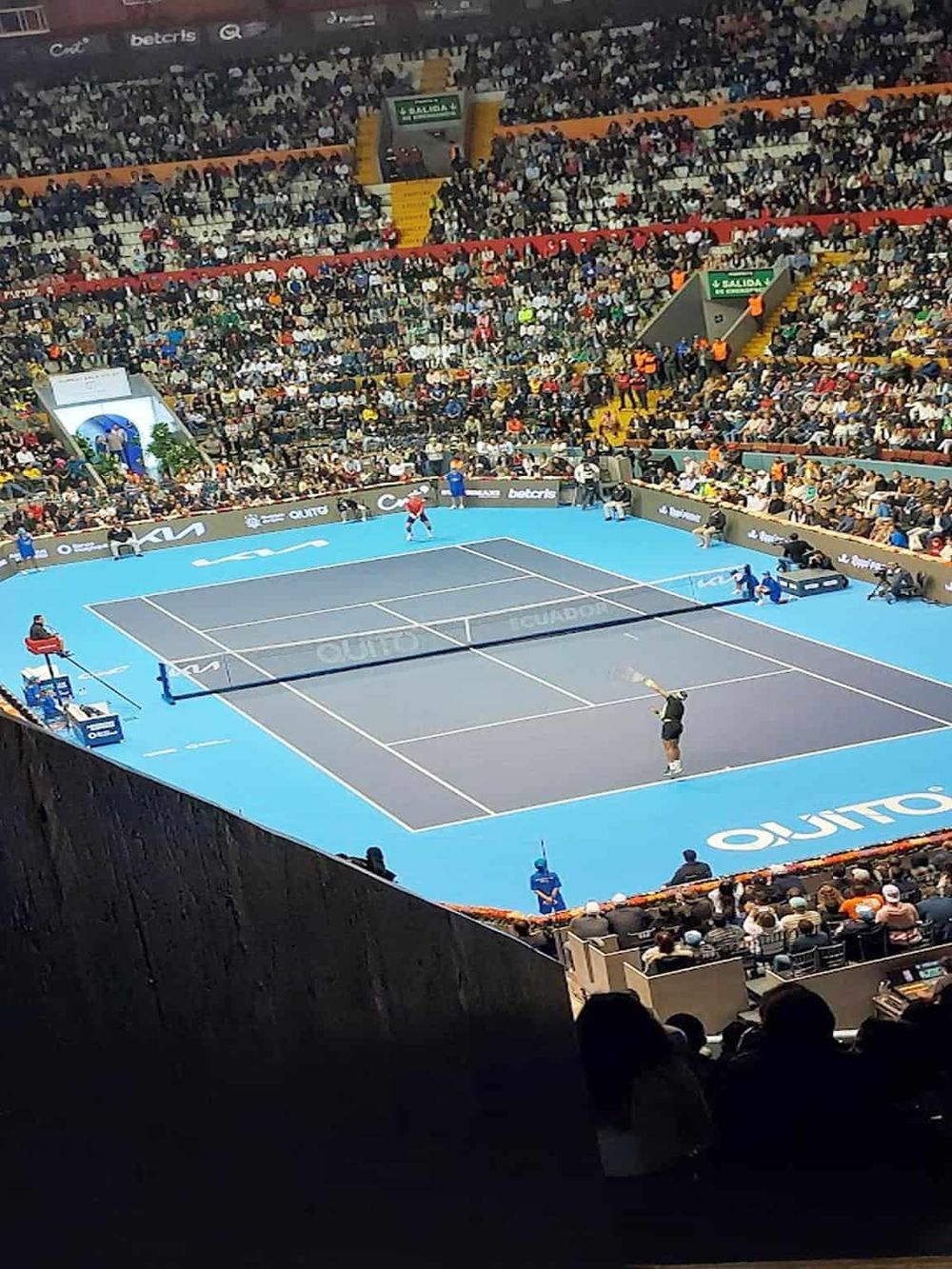 Colorful indoor tennis match in a packed stadium with vibrant audience.